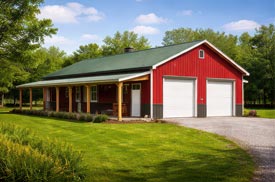 Custom post-frame building with red siding, green metal roof, and dual garage doors built for residential storage